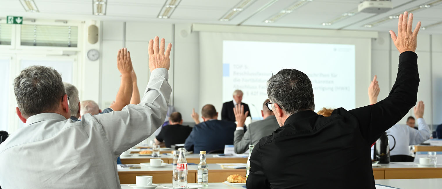 Foto von Mitgliedern der Vollversammlung, die die Hand zum Abstimmen heben