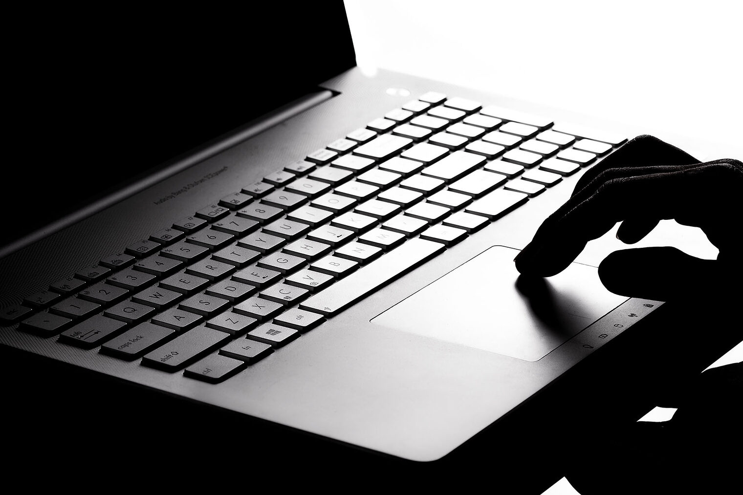 Dunkles Foto mit schwarzem Laptop und Hand im Schatten als Symbolbild für Cyber Crime