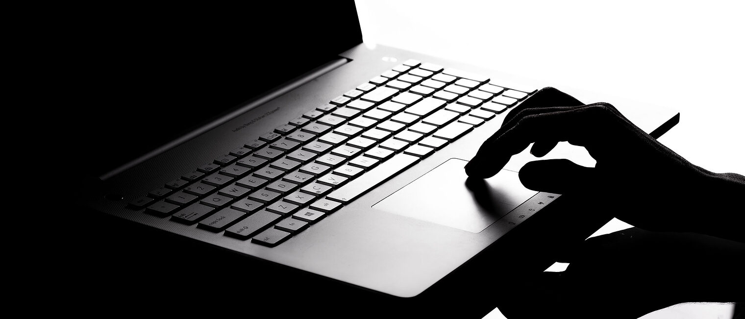 Symbolbild Hacker - Foto mit schwarzem Laptop und Hand im Schatten Dunkles Foto mit schwarzem Laptop und Hand im Schatten als Symbolbild für Cyber Crime