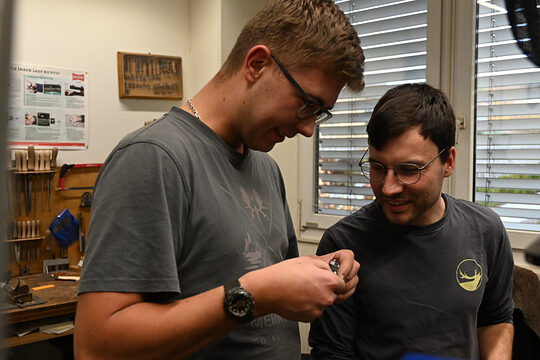 Zwei Männer in einer Werkstatt, schauen gemeinsam auf ein Werkstück
