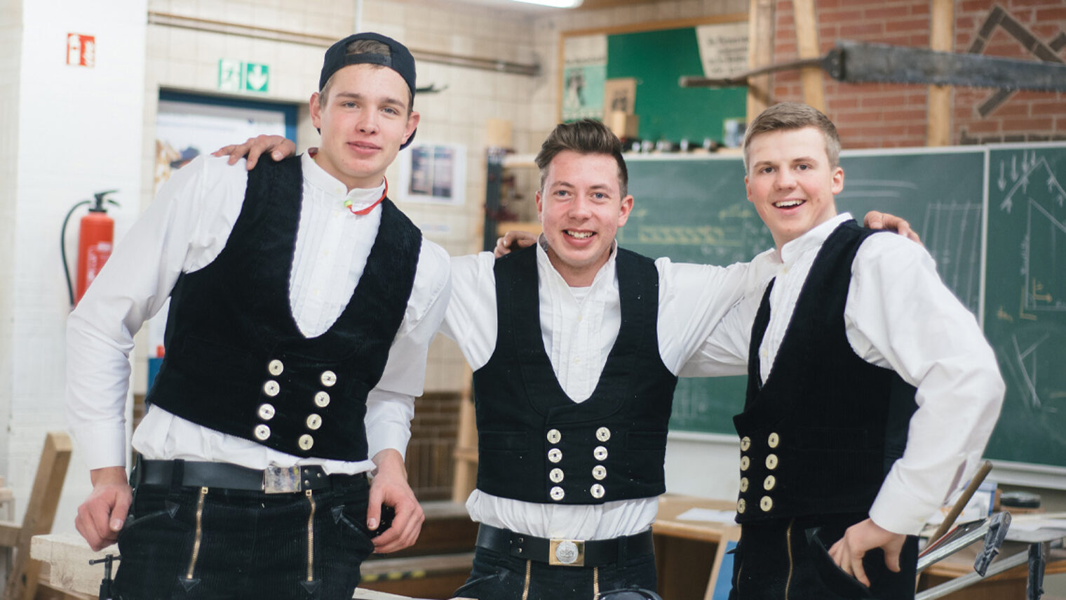 Drei Zimmerer in einer Werkstatt schauen freundschaftlich in die Kamera